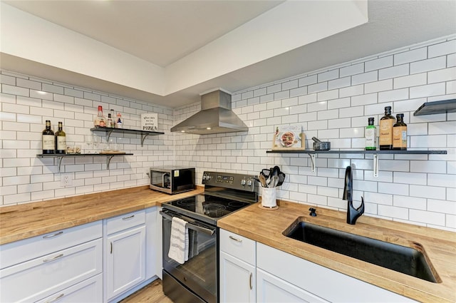 kitchen with wall chimney exhaust hood, butcher block counters, open shelves, and black range with electric stovetop