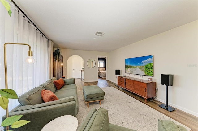 living room featuring arched walkways, visible vents, baseboards, and wood finished floors