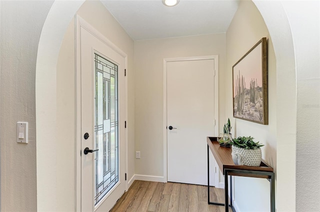 doorway to outside with arched walkways, baseboards, and light wood-style floors