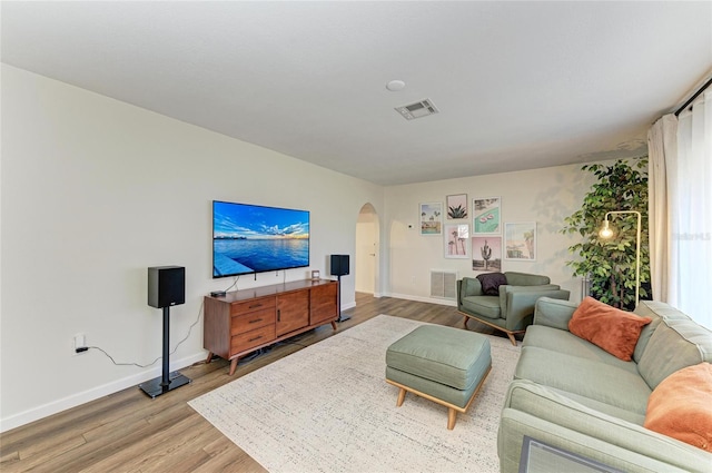 living room with light wood-style floors, baseboards, visible vents, and arched walkways