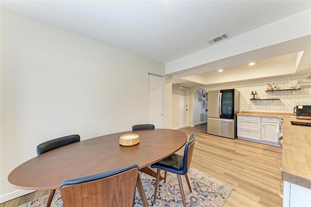 dining room with baseboards, visible vents, light wood-style flooring, a tray ceiling, and recessed lighting