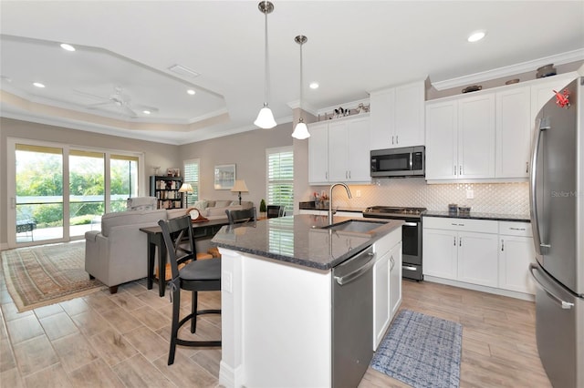 kitchen featuring sink, appliances with stainless steel finishes, dark stone countertops, hanging light fixtures, and a center island with sink