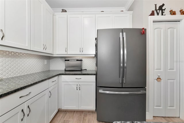 kitchen featuring stainless steel fridge, white cabinetry, tasteful backsplash, light hardwood / wood-style floors, and dark stone counters