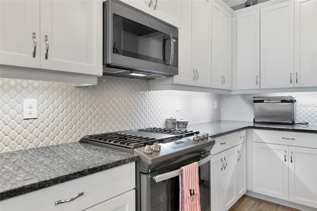kitchen with tasteful backsplash, dark stone countertops, stainless steel appliances, light hardwood / wood-style floors, and white cabinets