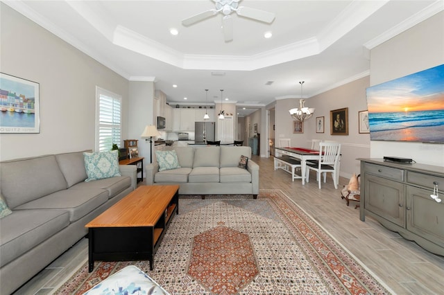 living room with a raised ceiling, crown molding, ceiling fan with notable chandelier, and light hardwood / wood-style flooring