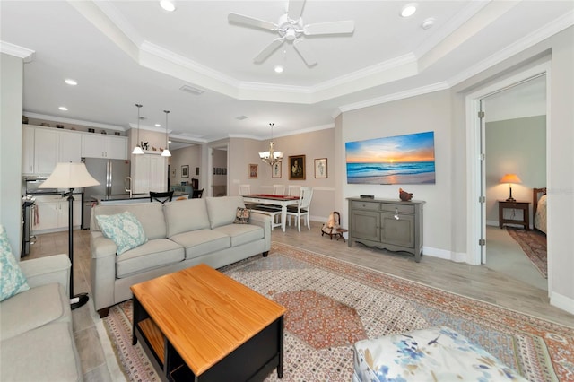 living room with a tray ceiling, ceiling fan with notable chandelier, ornamental molding, and light wood-type flooring