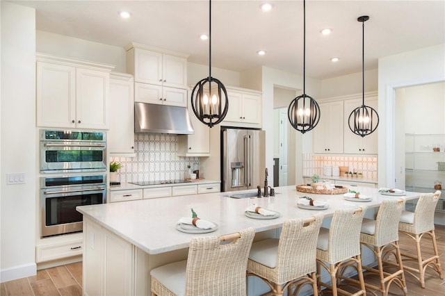 kitchen featuring stainless steel appliances, hanging light fixtures, and a center island with sink