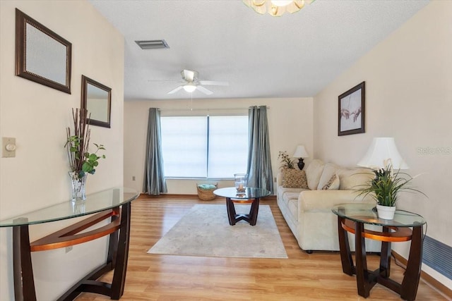 living room featuring ceiling fan, light hardwood / wood-style floors, and a textured ceiling