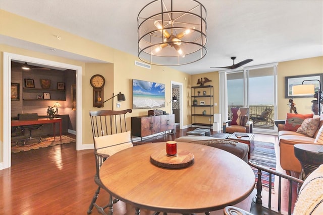 dining area with dark wood-type flooring, ceiling fan with notable chandelier, and a wall of windows