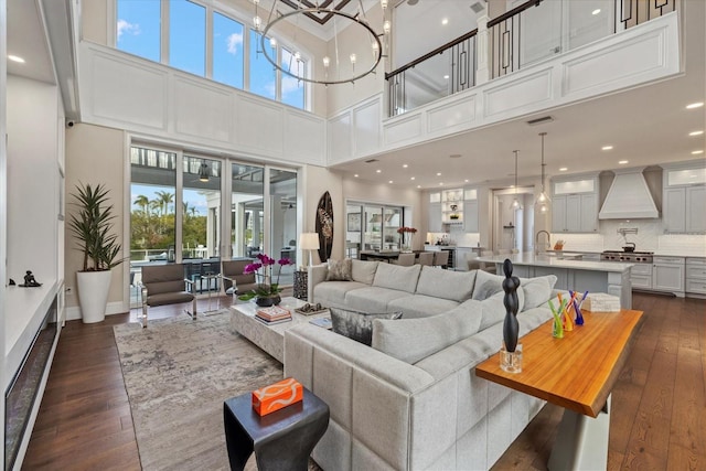 living room with sink, dark wood-type flooring, a towering ceiling, and a healthy amount of sunlight