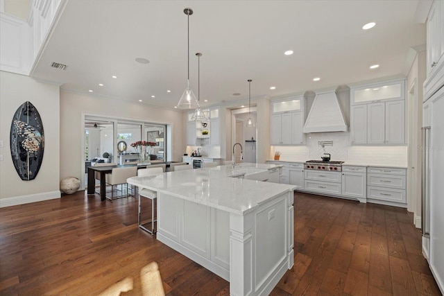 kitchen with light stone countertops, custom range hood, white cabinets, and a large island with sink