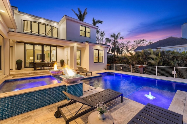 pool at dusk featuring an in ground hot tub, a patio, and an outdoor fire pit