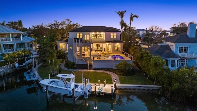 back house at dusk with a water view, a lawn, and a balcony