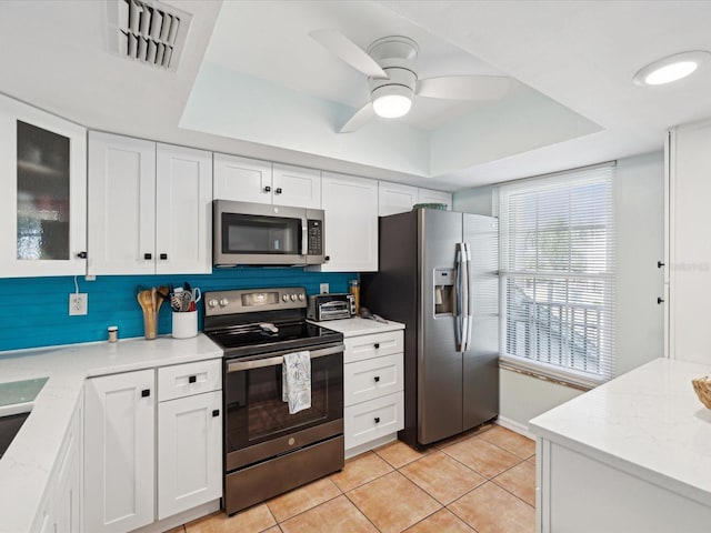 kitchen featuring appliances with stainless steel finishes, white cabinets, light stone counters, and a tray ceiling