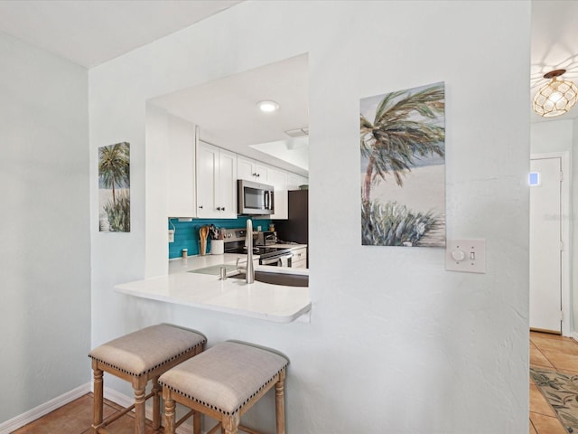 kitchen with baseboards, white cabinets, a breakfast bar, stainless steel appliances, and light countertops