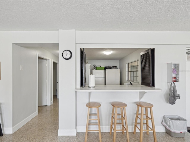 kitchen with a textured ceiling, a breakfast bar area, fridge, and freestanding refrigerator