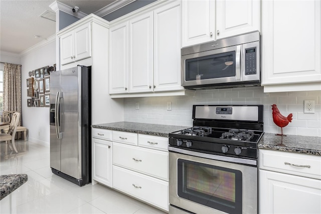 kitchen featuring white cabinetry, ornamental molding, appliances with stainless steel finishes, dark stone counters, and decorative backsplash