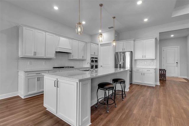 kitchen with premium range hood, pendant lighting, a center island with sink, and white cabinets