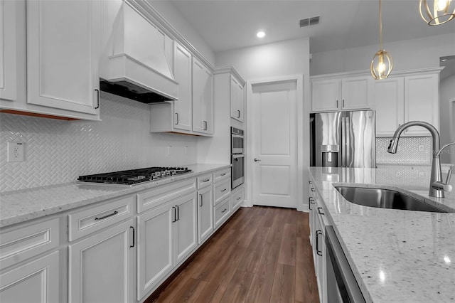 kitchen featuring sink, appliances with stainless steel finishes, premium range hood, hanging light fixtures, and white cabinets