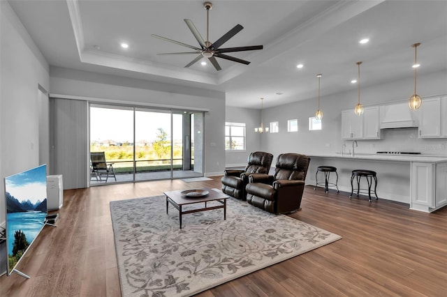 living room featuring hardwood / wood-style flooring, crown molding, ceiling fan with notable chandelier, and a tray ceiling