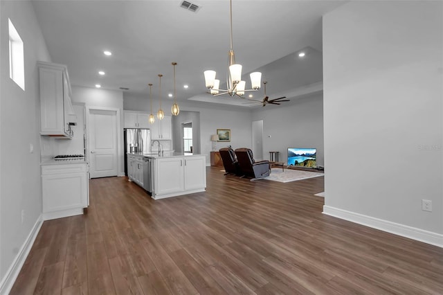 kitchen with dark wood-type flooring, white cabinetry, stainless steel appliances, a center island with sink, and decorative light fixtures