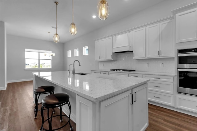 kitchen featuring sink, white cabinetry, a center island with sink, custom range hood, and stainless steel double oven