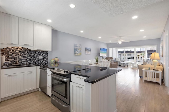 kitchen featuring open floor plan, appliances with stainless steel finishes, a peninsula, a ceiling fan, and a sink