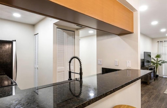 kitchen with dark stone countertops, dark hardwood / wood-style flooring, and stainless steel refrigerator