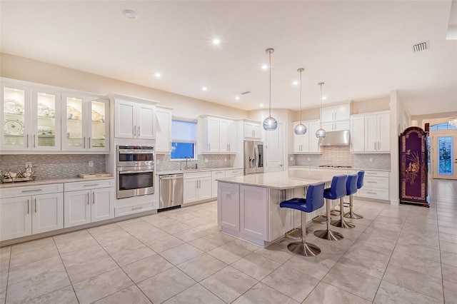 kitchen featuring a kitchen island, appliances with stainless steel finishes, white cabinets, and decorative light fixtures