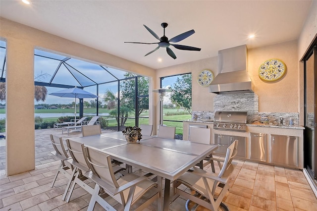 view of patio featuring area for grilling, a water view, glass enclosure, and an outdoor kitchen