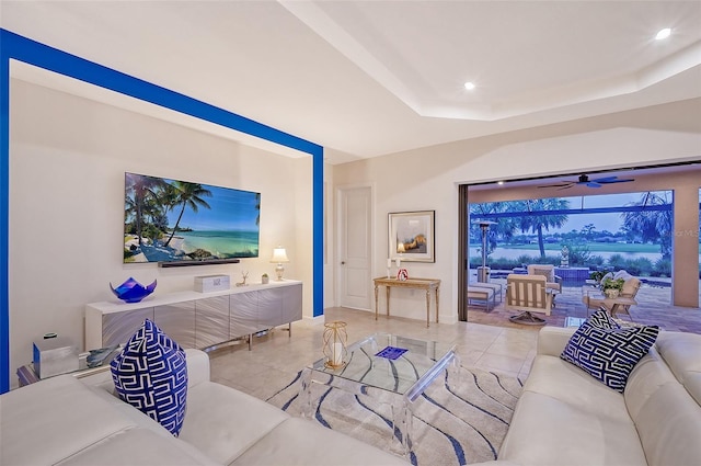 tiled living room with ceiling fan and a tray ceiling