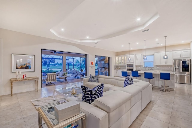 living room featuring a raised ceiling, plenty of natural light, sink, and light tile patterned floors