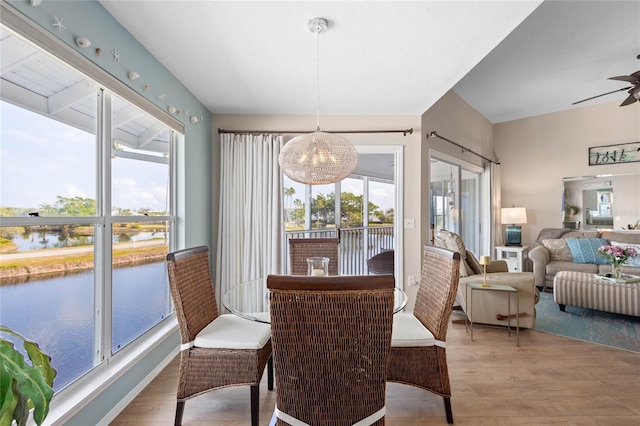 dining area featuring ceiling fan with notable chandelier, a water view, and hardwood / wood-style floors