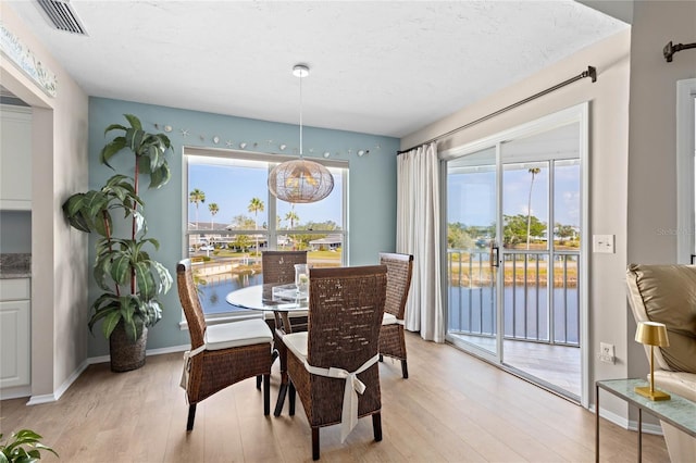 dining space featuring light hardwood / wood-style floors, a textured ceiling, and a water view