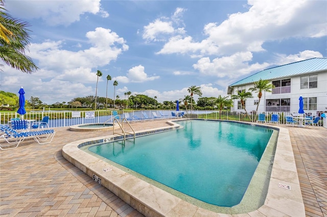 view of swimming pool featuring a water view, a hot tub, and a patio area