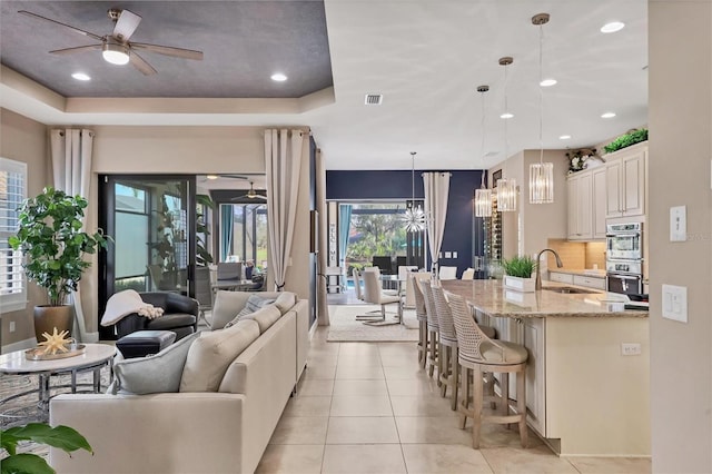 living room with a raised ceiling, light tile patterned floors, ceiling fan, and sink