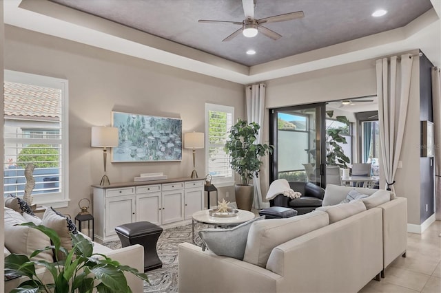 living room with light tile patterned flooring, ceiling fan, and a tray ceiling