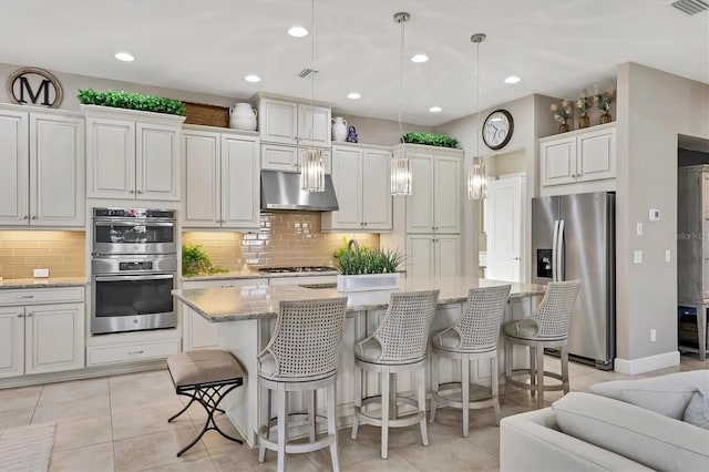 kitchen with white cabinetry, stainless steel appliances, pendant lighting, and an island with sink