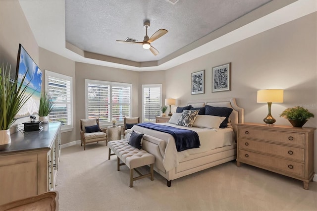 carpeted bedroom with ceiling fan, a tray ceiling, and a textured ceiling