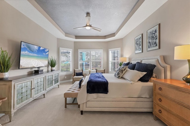 bedroom with a tray ceiling, light carpet, a textured ceiling, and ceiling fan