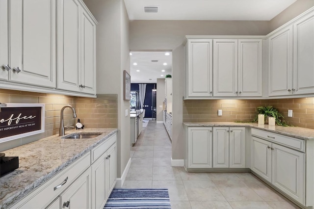 kitchen with sink, white cabinets, light stone countertops, and light tile patterned floors