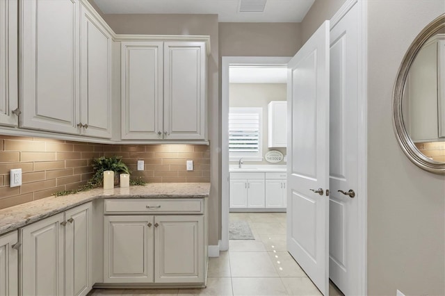 kitchen featuring decorative backsplash, light tile patterned floors, white cabinetry, and light stone counters