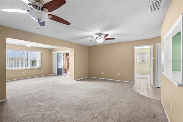 empty room featuring light colored carpet, visible vents, light tile patterned flooring, ceiling fan, and a textured ceiling