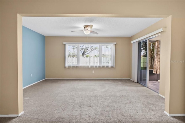 empty room with a ceiling fan, light colored carpet, a textured ceiling, and baseboards