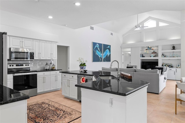 kitchen featuring sink, stainless steel appliances, an island with sink, white cabinets, and dark stone counters