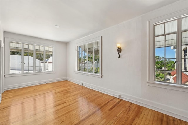 unfurnished room featuring wood finished floors, baseboards, and a healthy amount of sunlight