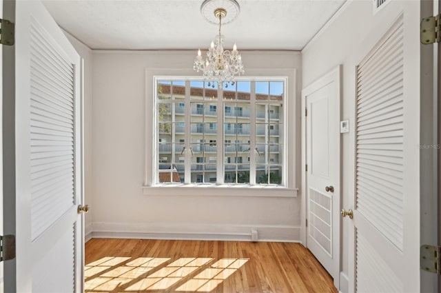 interior space with baseboards, an inviting chandelier, light wood-style flooring, and ornamental molding