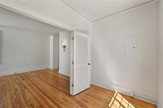 spare room featuring electric panel, baseboards, and light wood finished floors