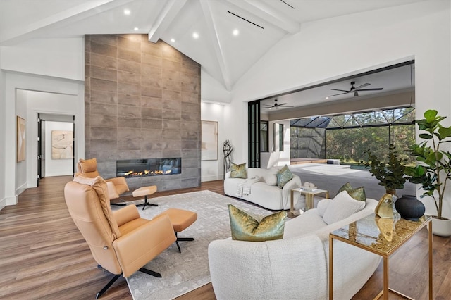 living room with wood-type flooring, beam ceiling, a tiled fireplace, and high vaulted ceiling