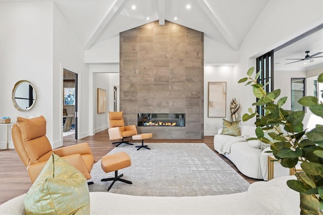 living room featuring high vaulted ceiling, a tile fireplace, beamed ceiling, and light wood-type flooring